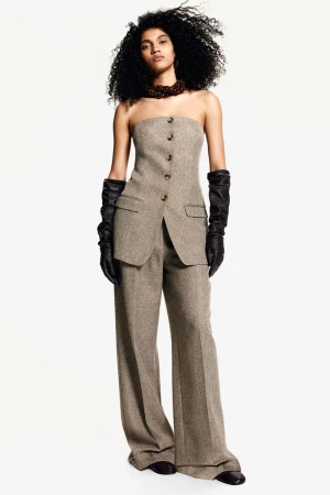 Model in strapless beige tweed top and matching trousers wearing black leather opera gloves against a white seamless backdrop