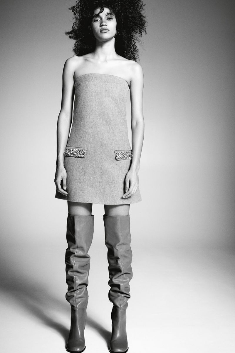 Model in strapless mini dress and over-the-knee boots standing against a neutral studio backdrop