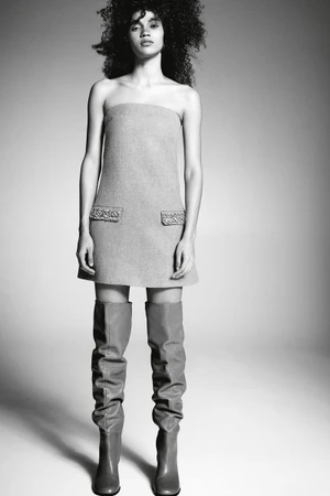 Model in strapless mini dress and over-the-knee boots standing against a neutral studio backdrop
