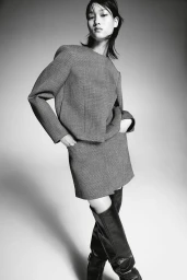 Model in grey tailored co-ord skirt suit and dark knee-high boots posing against a neutral gradient backdrop