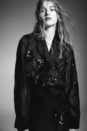 Model in a dark embroidered blouse against a grey seamless background for H&M autumn winter campaign