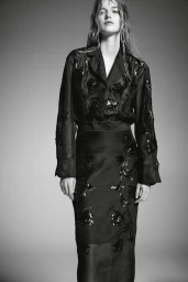 Model in black floral embroidered blouse and matching skirt against grey seamless studio background