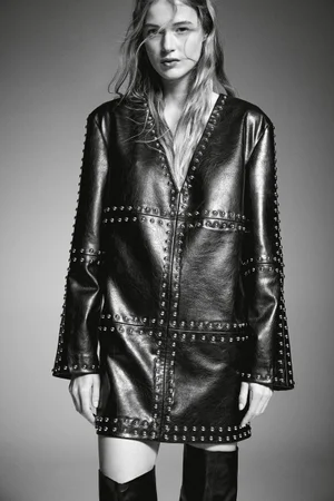 Model in a studded black leather dress and knee-high boots against a grey studio backdrop for H&M A/W 2024 lookbook