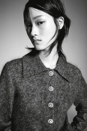 Model in a textured dark grey button-up collared top against a plain studio background.