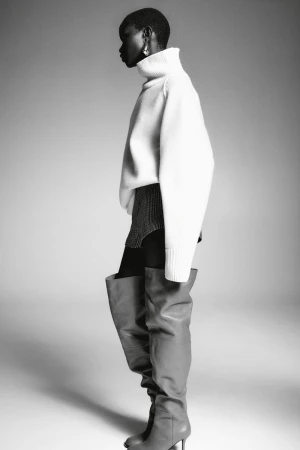 Model Akon Changkou wearing a white turtleneck sweater and tall boots against a neutral studio backdrop