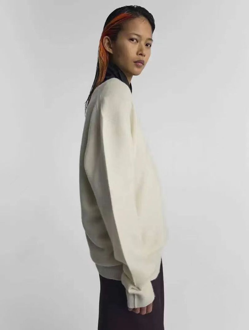 Studio shot of an Asian woman in a cream sweater and brown skirt, looking over her shoulder with colored streaks in her hair.