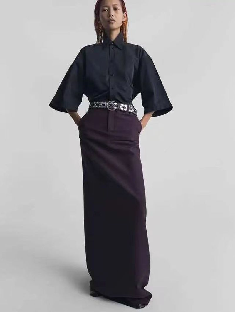 Full shot of an East Asian female model in a dark short-sleeved shirt and long skirt, posing against a neutral backdrop in a studio.
