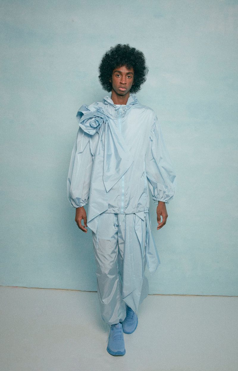 Fashion model in light blue jacket and pants walking on a light blue background in studio for fashion editorial content creation, posing.