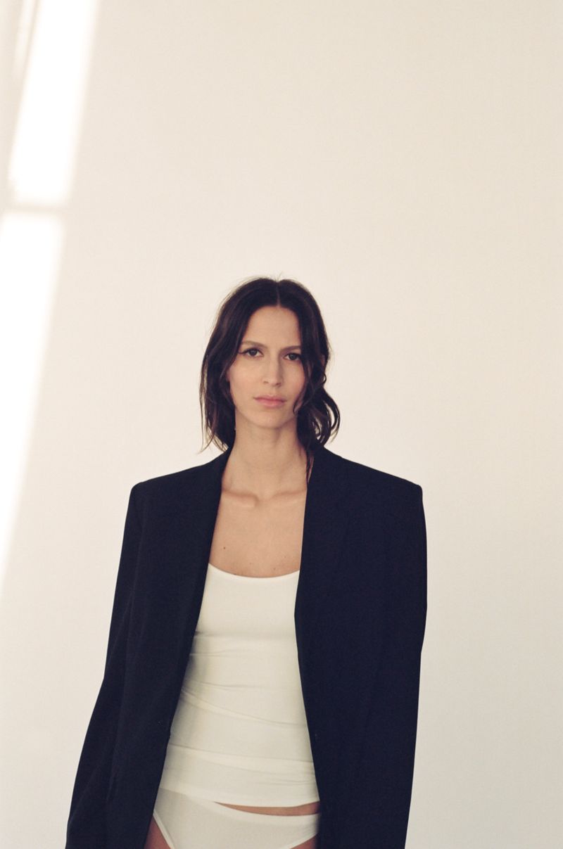 Jeanne Cadieu wearing an oversized black blazer and white tank top against a minimalist white studio background.