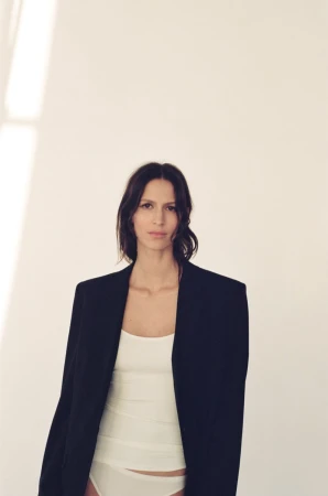 Jeanne Cadieu wearing an oversized black blazer and white tank top against a minimalist white studio background.