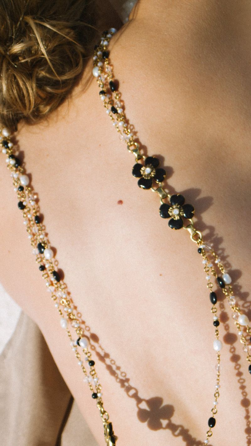 Close-up on an adult female's back and shoulders, adorned with a beaded gold necklace featuring black flower-shaped embellishments.