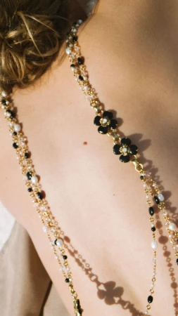 Close-up on an adult female's back and shoulders, adorned with a beaded gold necklace featuring black flower-shaped embellishments.