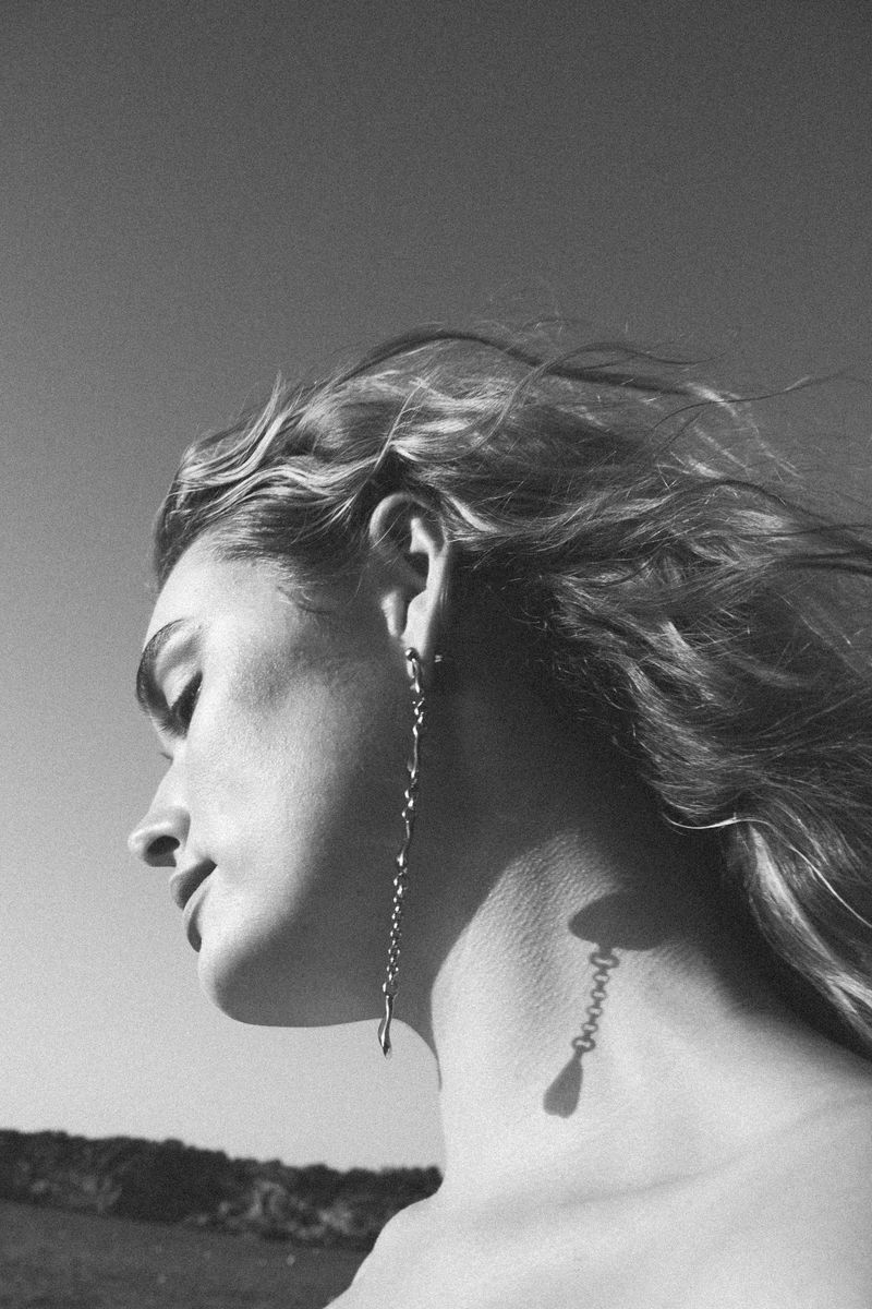 Profile view of a fair-skinned woman with blonde hair and long dangling earrings. The sky is visible in the black and white photo.