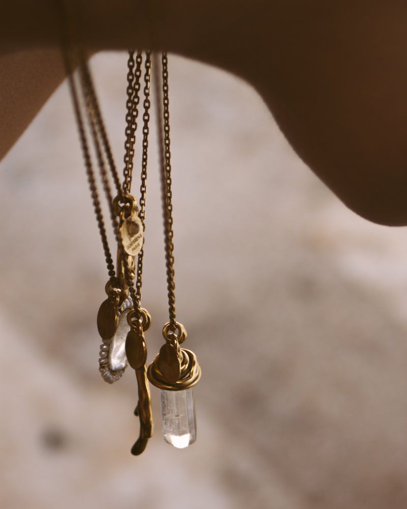 Elegant jewelry display featuring three necklaces with delicate brass chains and natural crystal pendants hanging against a soft backdrop.