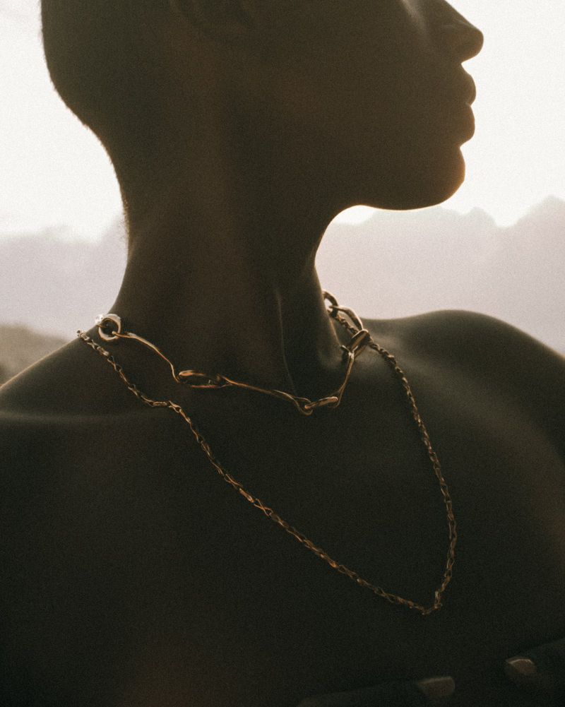 Close-up silhouette of an adult female wearing a golden chain necklace with a natural outdoor background at daytime.