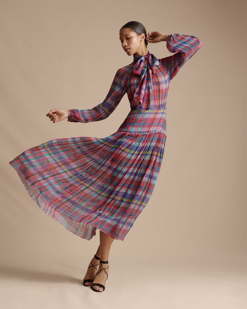 An Asian woman is posing in a flowing plaid dress in a studio with soft lighting, creating a visually striking fashion photograph.