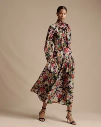 Model wearing a long sleeve floral print dress with a high neck tie against a neutral background.