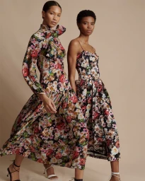 Two models wearing floral print midi dresses and strappy high heels posing against a warm neutral studio backdrop.