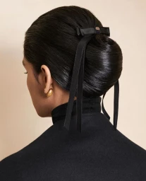 Rear view of a person with glossy dark hair styled in an elegant bun secured with a black ribbon bow and a gold earring.