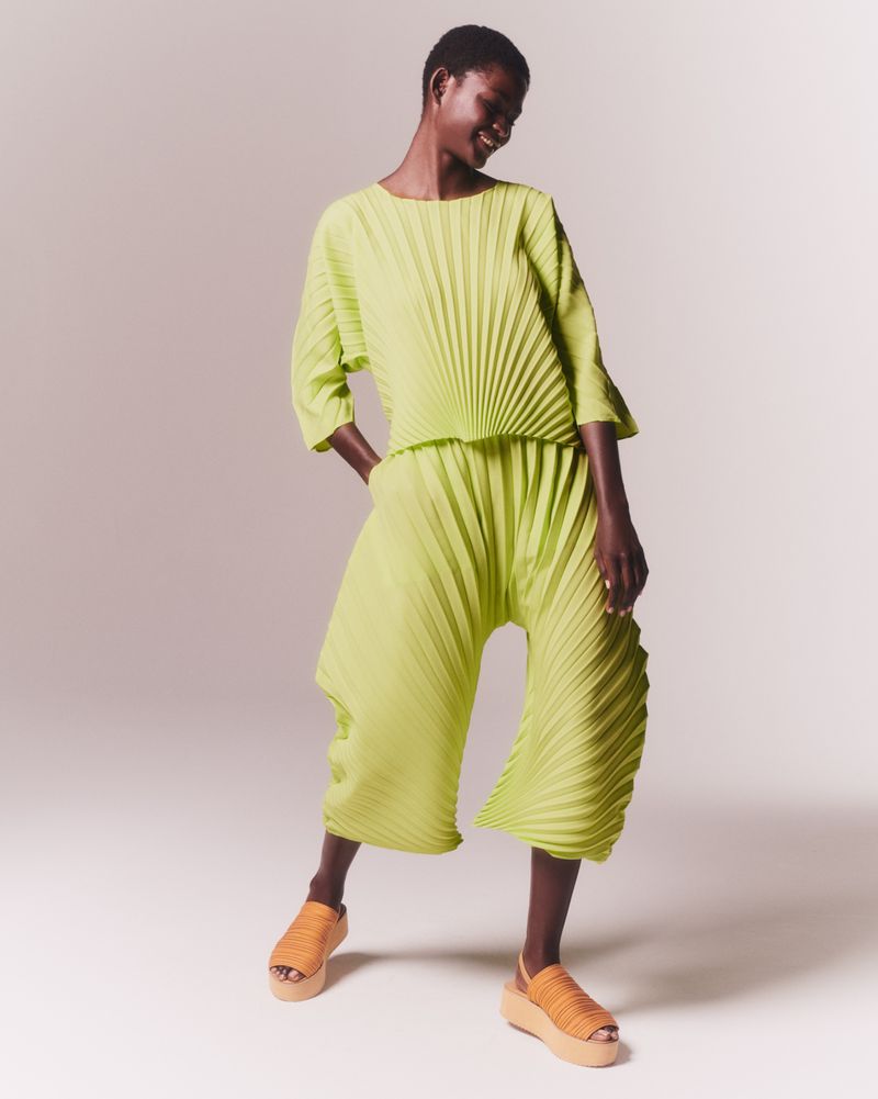Full-length shot of an adult African-descent woman smiling and posing in pleated chartreuse matching separates and platform sandals against white.
