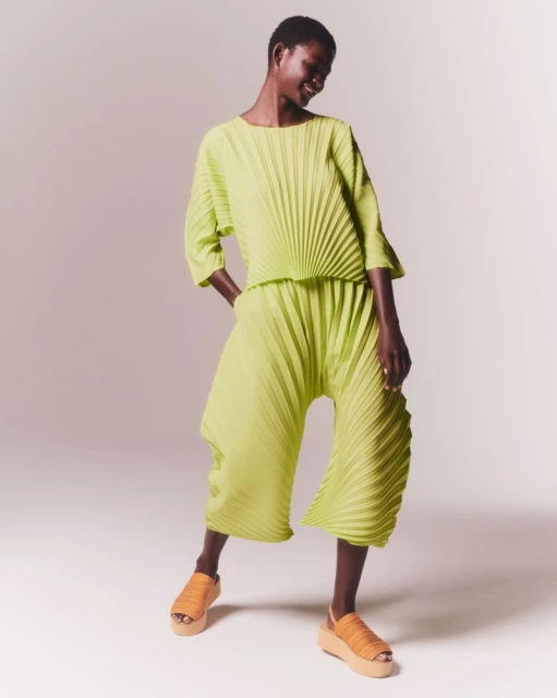 Full-length shot of an adult African-descent woman smiling and posing in pleated chartreuse matching separates and platform sandals against white.