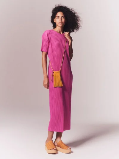 Model in pink pleated dress and platform sandals wearing a small yellow cross-body bag against a plain studio background