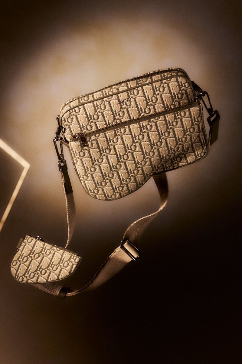 Elevated product shot of a cream and brown Dior Oblique jacquard print cross body bag with a saddle bag accessory, set against a tan gradient.