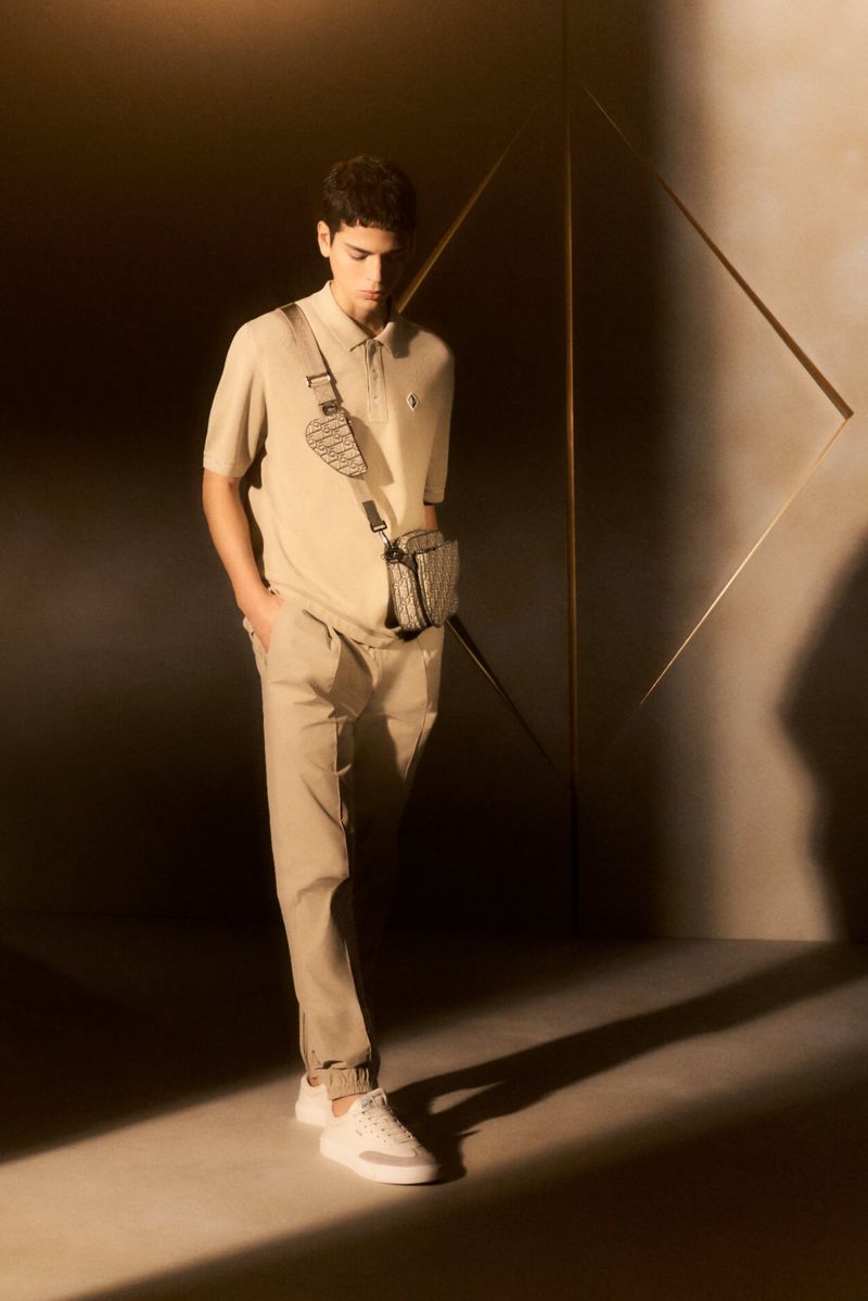 Tobias Baez in a beige polo shirt and matching trousers with a Dior crossbody bag in warm geometric set lighting.