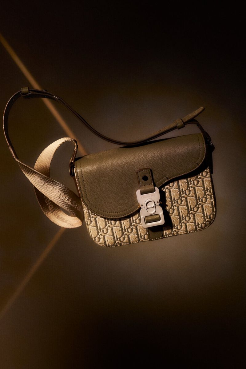 Olive green Dior saddle bag with beige monogram print, silver hardware, and an adjustable strap, showcased against a dark backdrop.