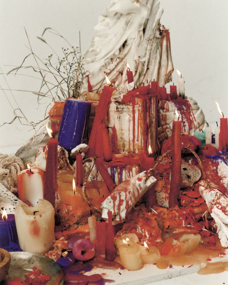 Still life with melting candles, white cloth, and organic materials creating an ephemeral, textured composition against a light background.