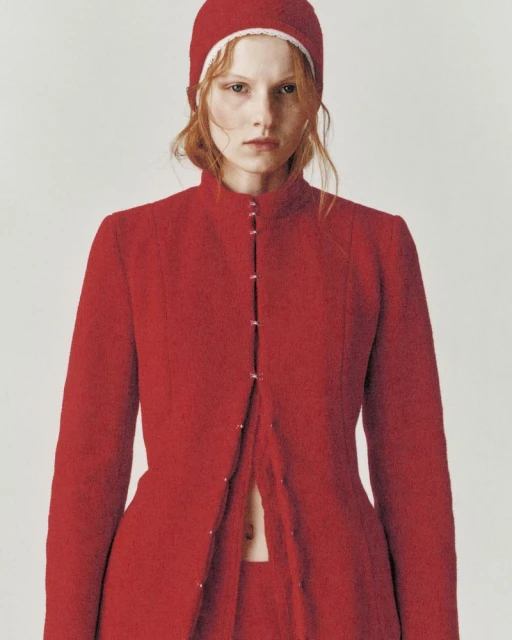 Fashion portrait of a redhead woman wearing a red coat and matching hat, set against a neutral backdrop in a studio environment.