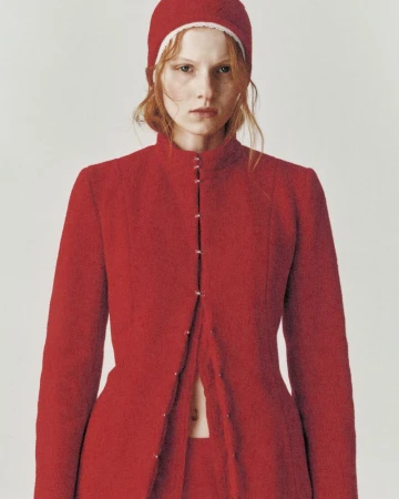 Fashion portrait of a redhead woman wearing a red coat and matching hat, set against a neutral backdrop in a studio environment.