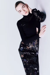 Model Nariah Nicolle leaning against a white wall wearing a black ribbed turtleneck and sequined skirt for Cristiano Burani FW24.