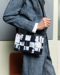 Model wearing blue textured jacket and trousers carrying a black and white woven leather handbag