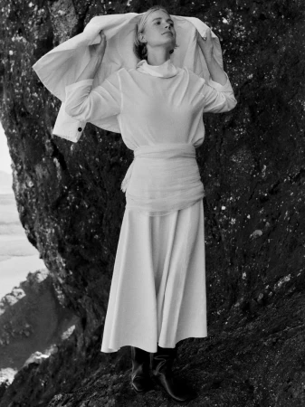 Monochrome fashion portrait of a model standing against a dark rocky terrain holding up a light jacket