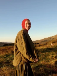 Model wearing an olive quilted jacket and red headscarf standing in a grassy field at sunset for Massimo Dutti.
