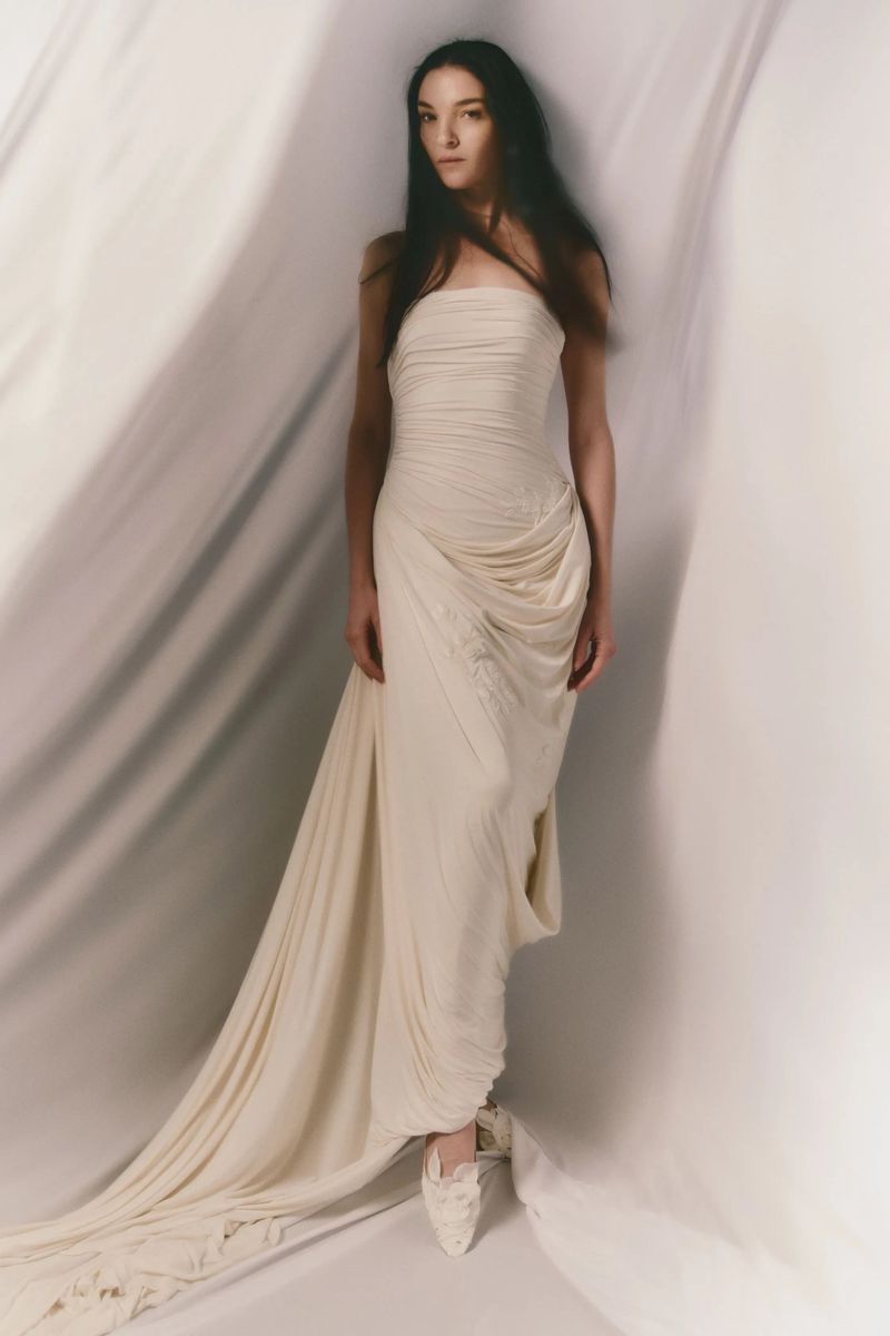 Elegant woman in strapless gown poses in a photo studio with draped fabric background, showcasing a timeless bridal or fashion aesthetic.