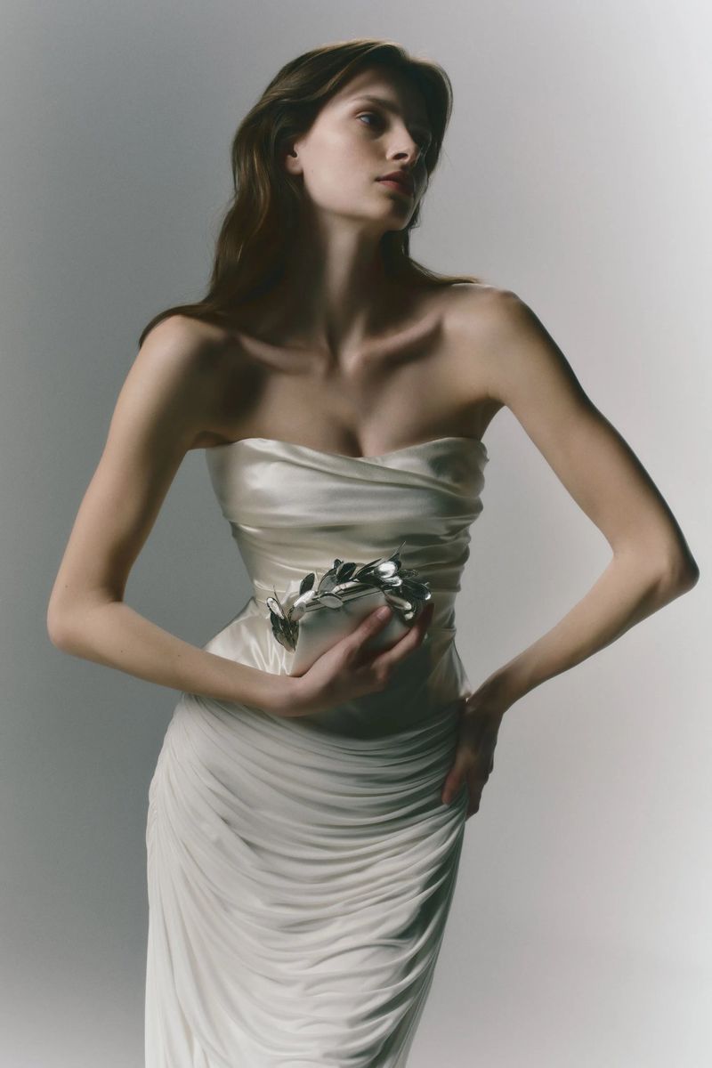 Elegant brunette woman in a strapless white gown holding a decorative object in a photo studio with soft, diffused lighting.