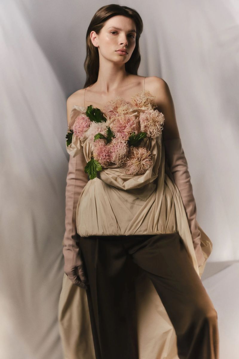Elegant woman in a beige dress with floral details and long gloves, posing in a photo studio with soft, diffused lighting and a clean backdrop.