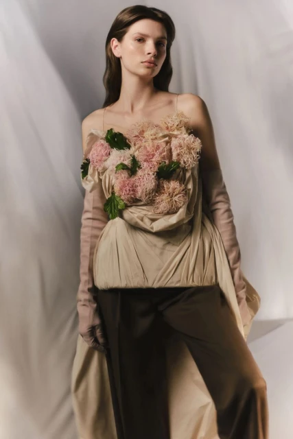 Elegant woman in a beige dress with floral details and long gloves, posing in a photo studio with soft, diffused lighting and a clean backdrop.