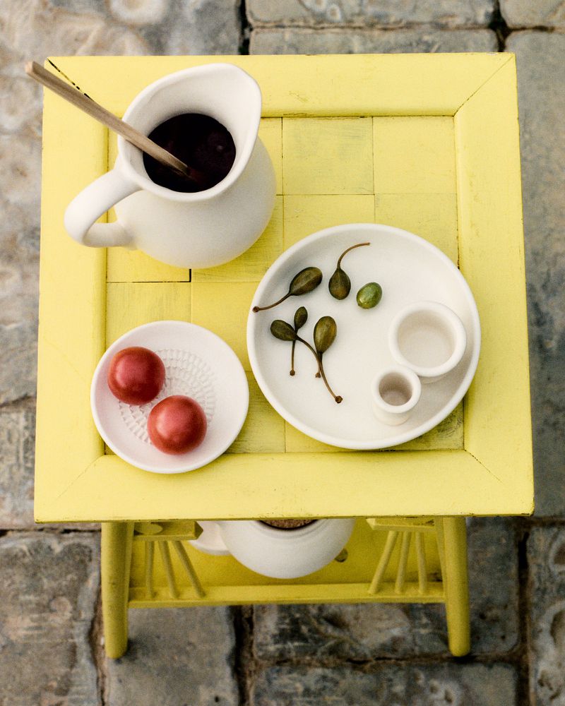 Overhead shot of yellow table with tomato appetizers, olives, sauce in white serving dishes, and a wooden spoon for bright, clean food photography.