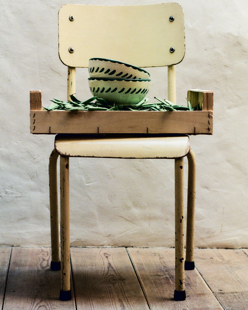 Still life featuring bowls on a wooden tray, which sits on a yellow vintage school chair against a textured beige background and wood floor.
