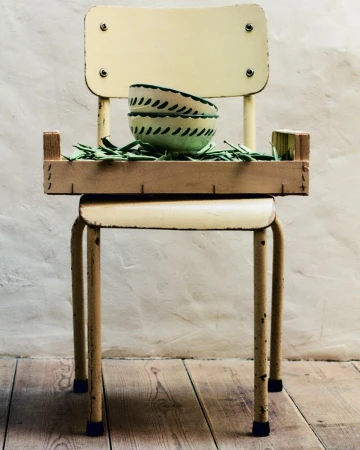 Still life featuring bowls on a wooden tray, which sits on a yellow vintage school chair against a textured beige background and wood floor.