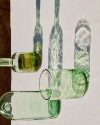 Green glass bottles and a glass casting intricate caustic light patterns onto a white surface