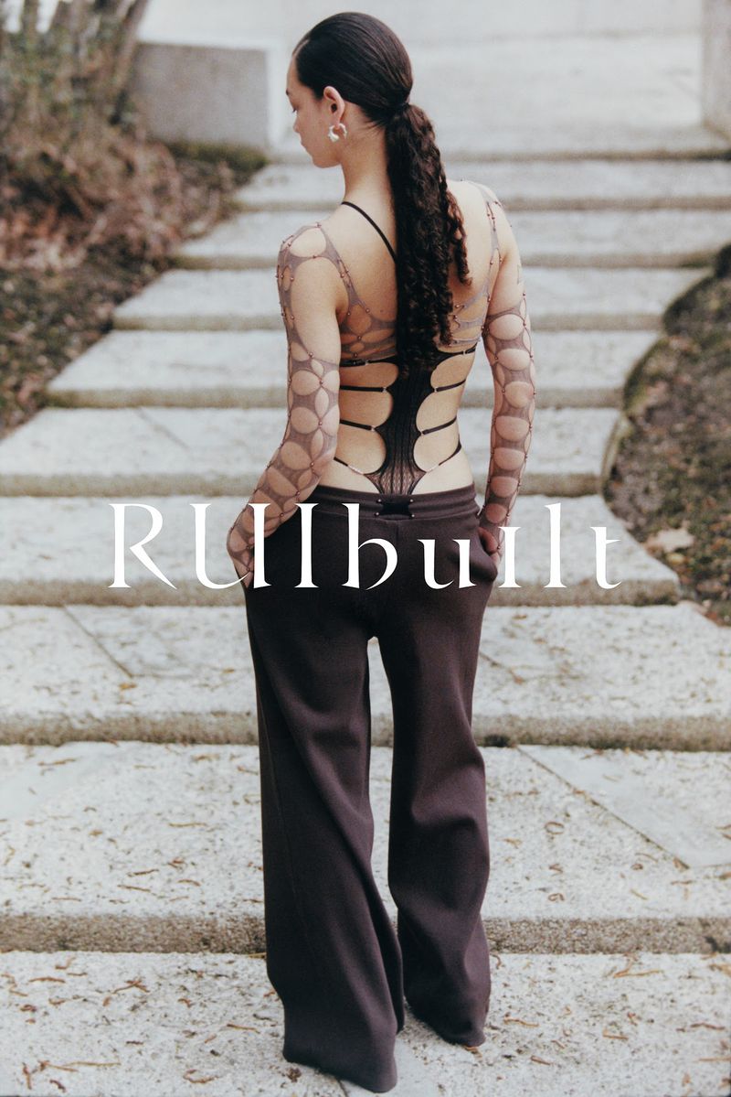 Woman in open-back top and trousers stands on stone steps outdoors, fashion-forward style, minimalist aesthetic, and natural light.