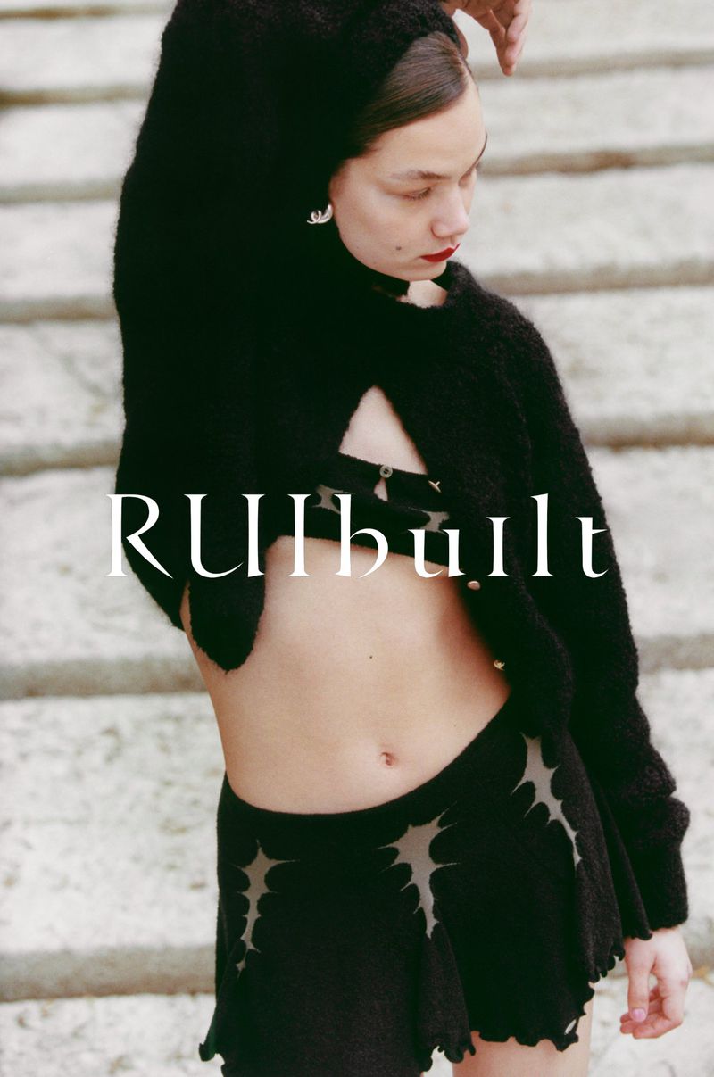 Woman in a black knit cardigan and skirt with cutout details poses against a light stone staircase, showcasing high-fashion style.