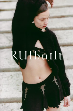 Woman in a black knit cardigan and skirt with cutout details poses against a light stone staircase, showcasing high-fashion style.