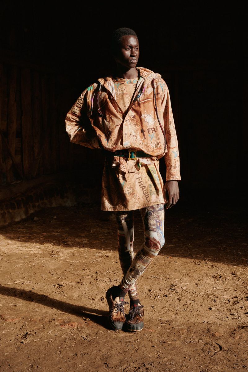 An adult model poses in a hooded jacket, belted mini-skirt, printed leggings and lug-sole shoes, set against a dark indoor background.