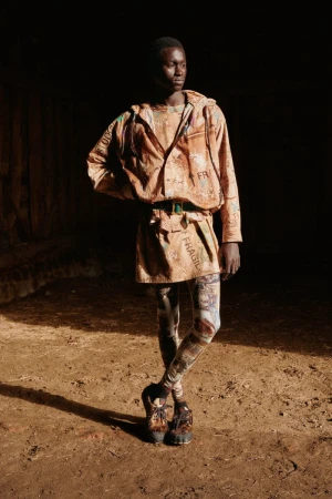 An adult model poses in a hooded jacket, belted mini-skirt, printed leggings and lug-sole shoes, set against a dark indoor background.