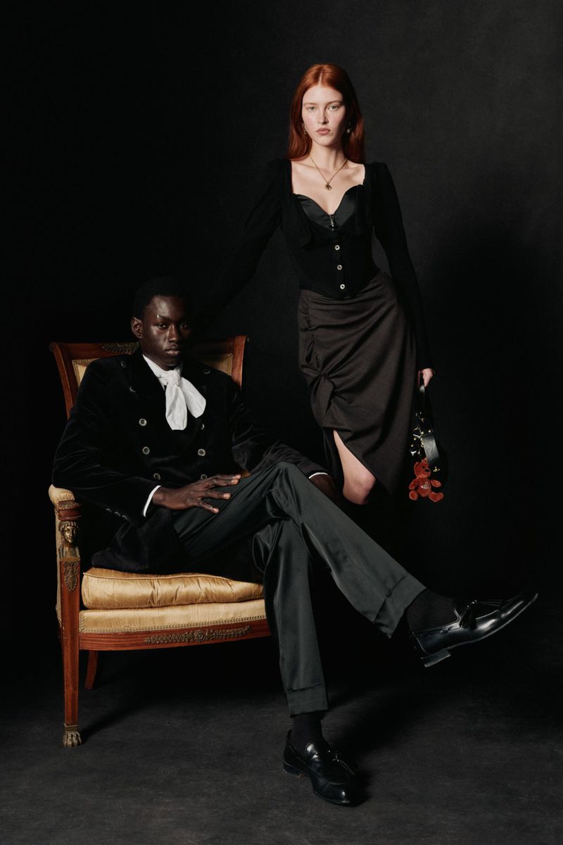 Elegant fashion portrait of an African American man seated next to a red-haired white woman in formal wear against a dark background.